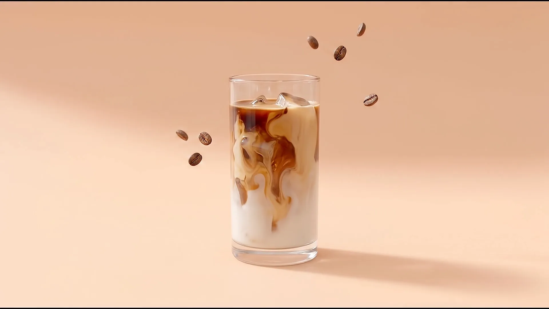 A tall glass of iced latte on a peach backdrop, espresso marbled through cold milk and ice, coffee beans floating beside it.
